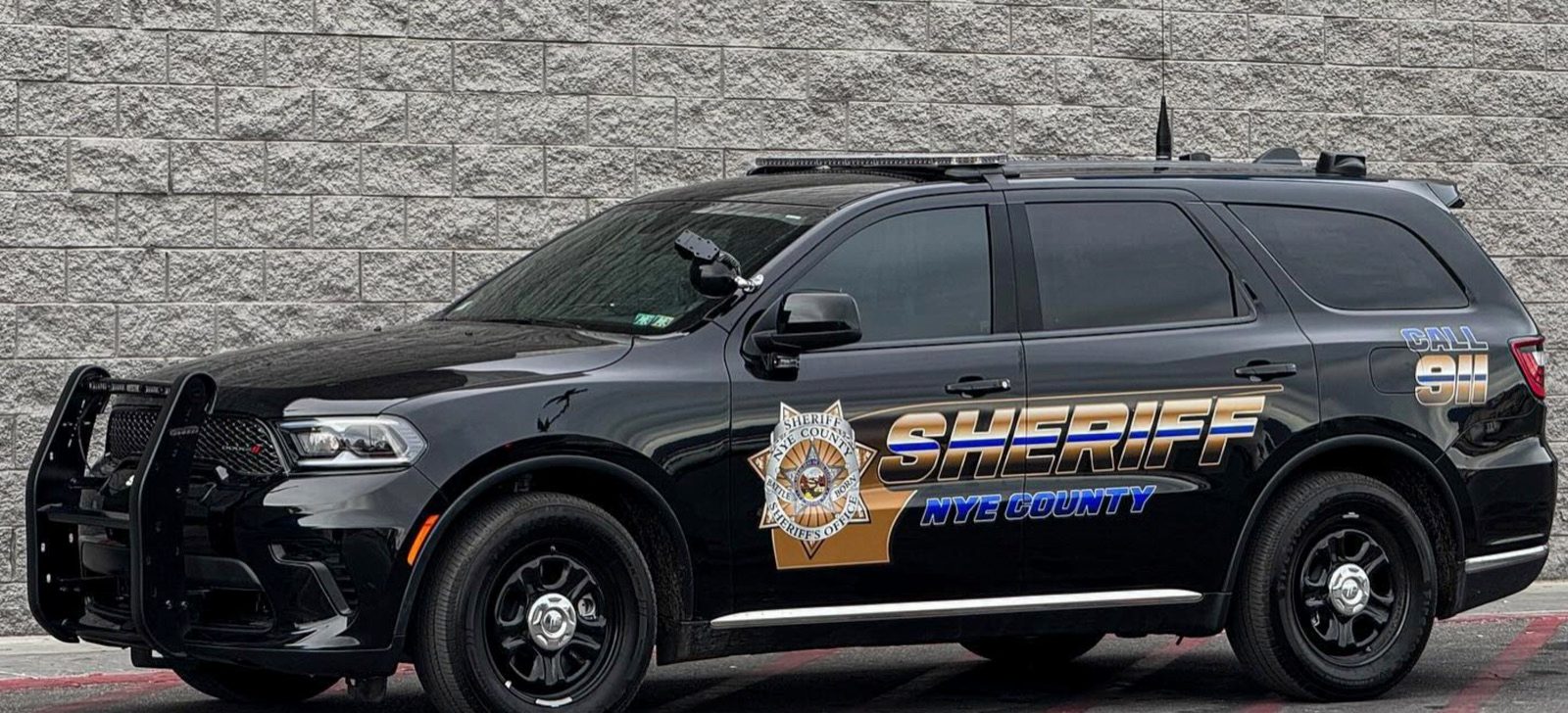 A Nye County Sheriff's Office patrol vehicle, a black Dodge Durango marked Sheriff, Nye County, parked against a block wall.